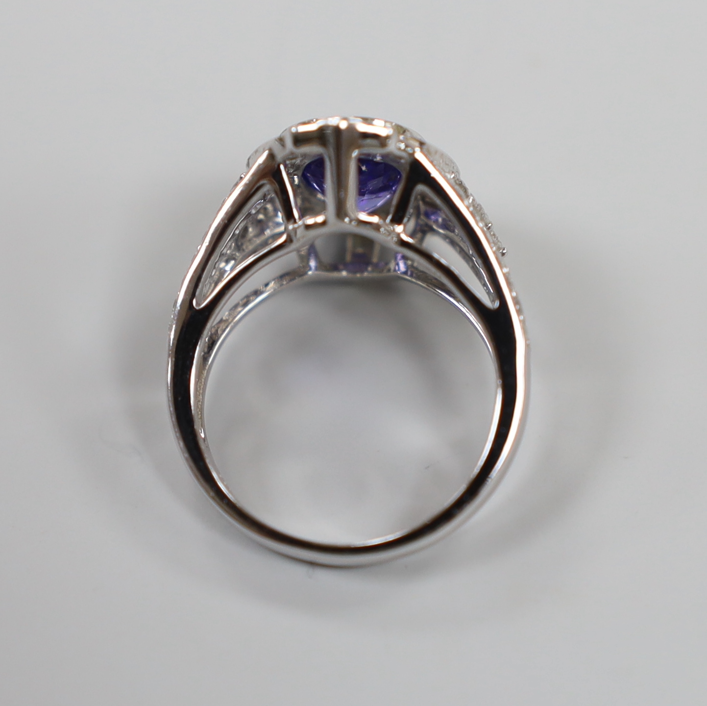 A modern 14k white metal, oval cut tanzanite and diamond chip set cluster dress ring, with diamond chip set shoulders, size M, gross weight 7 grams.